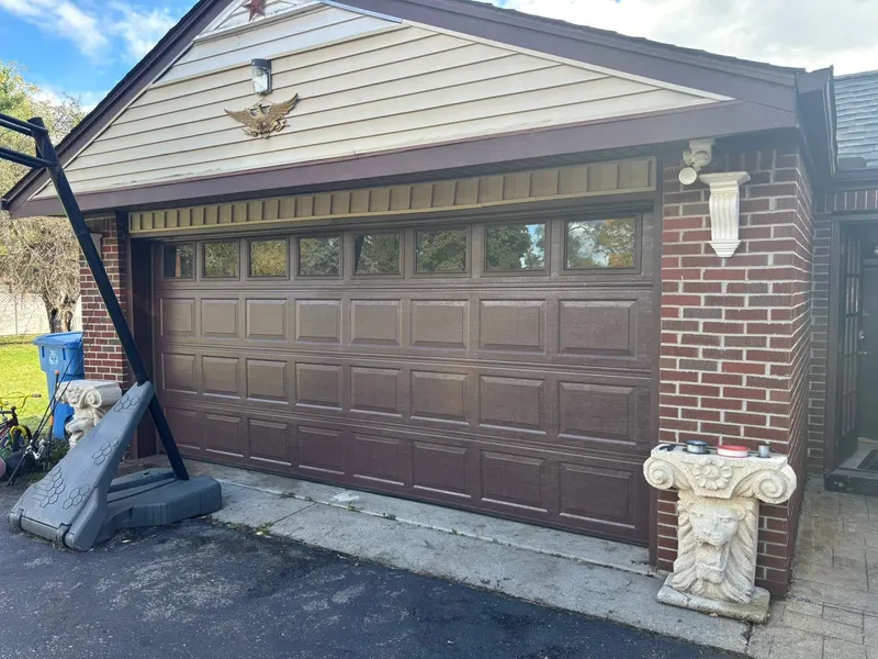 Brown raised-panel double garage door with a row of windows across the top section