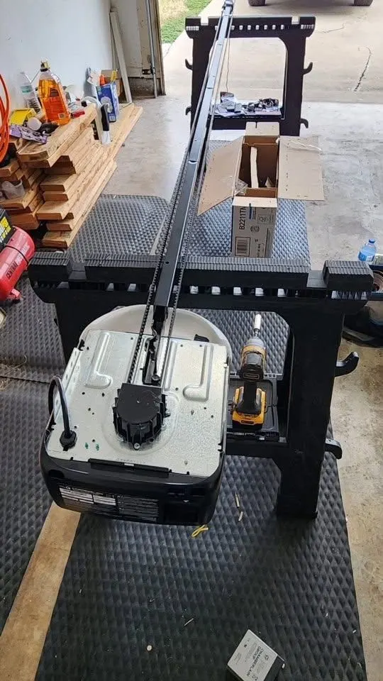 New garage door opener and rail being assembled on sawhorses inside a garage, with a drill and the parts box