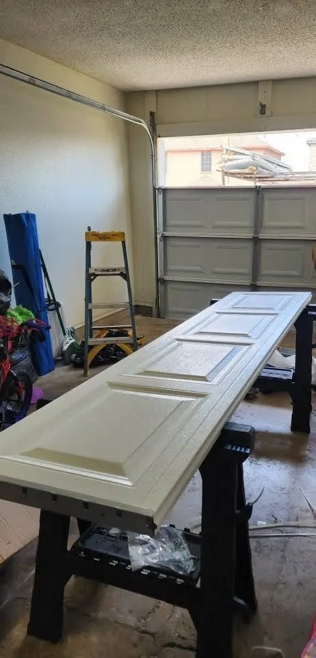 New white raised-panel garage door section on sawhorses, with the door missing that section behind it