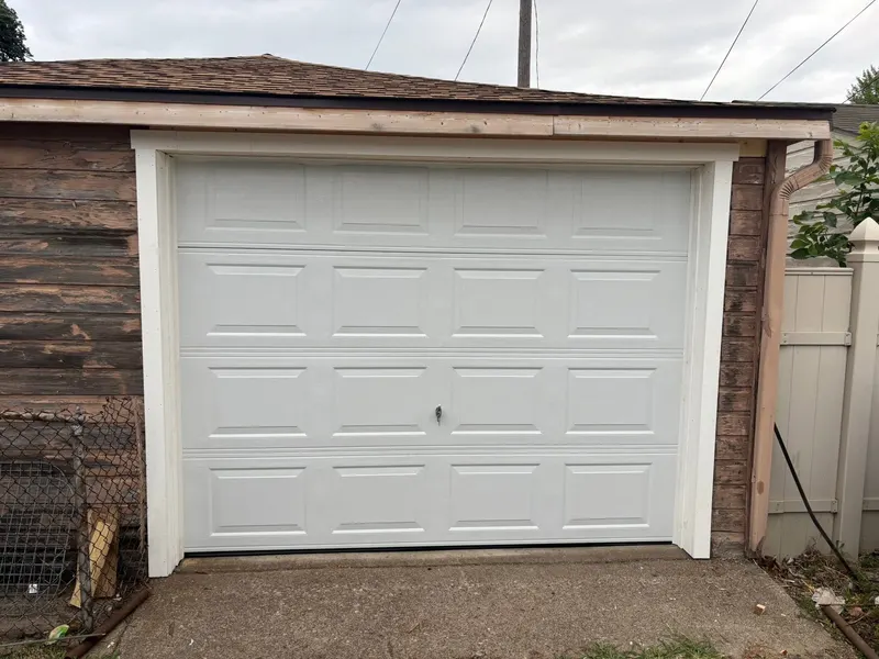 New white raised-panel single garage door with new white trim on a detached garage