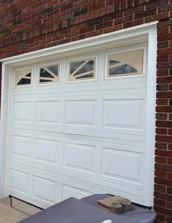 White raised-panel garage door with sunburst windows on a brick house