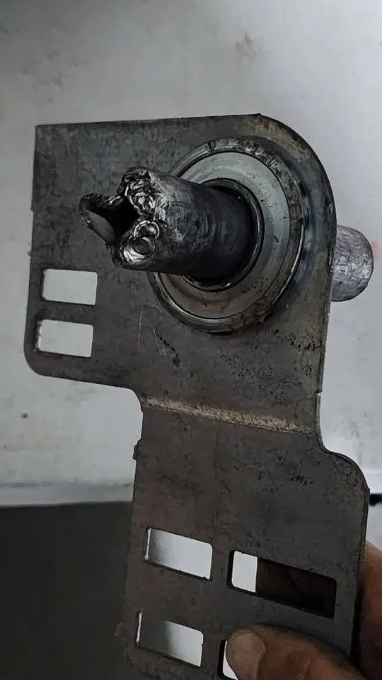 Worn garage door end bearing plate with a damaged torsion shaft end, held in a hand